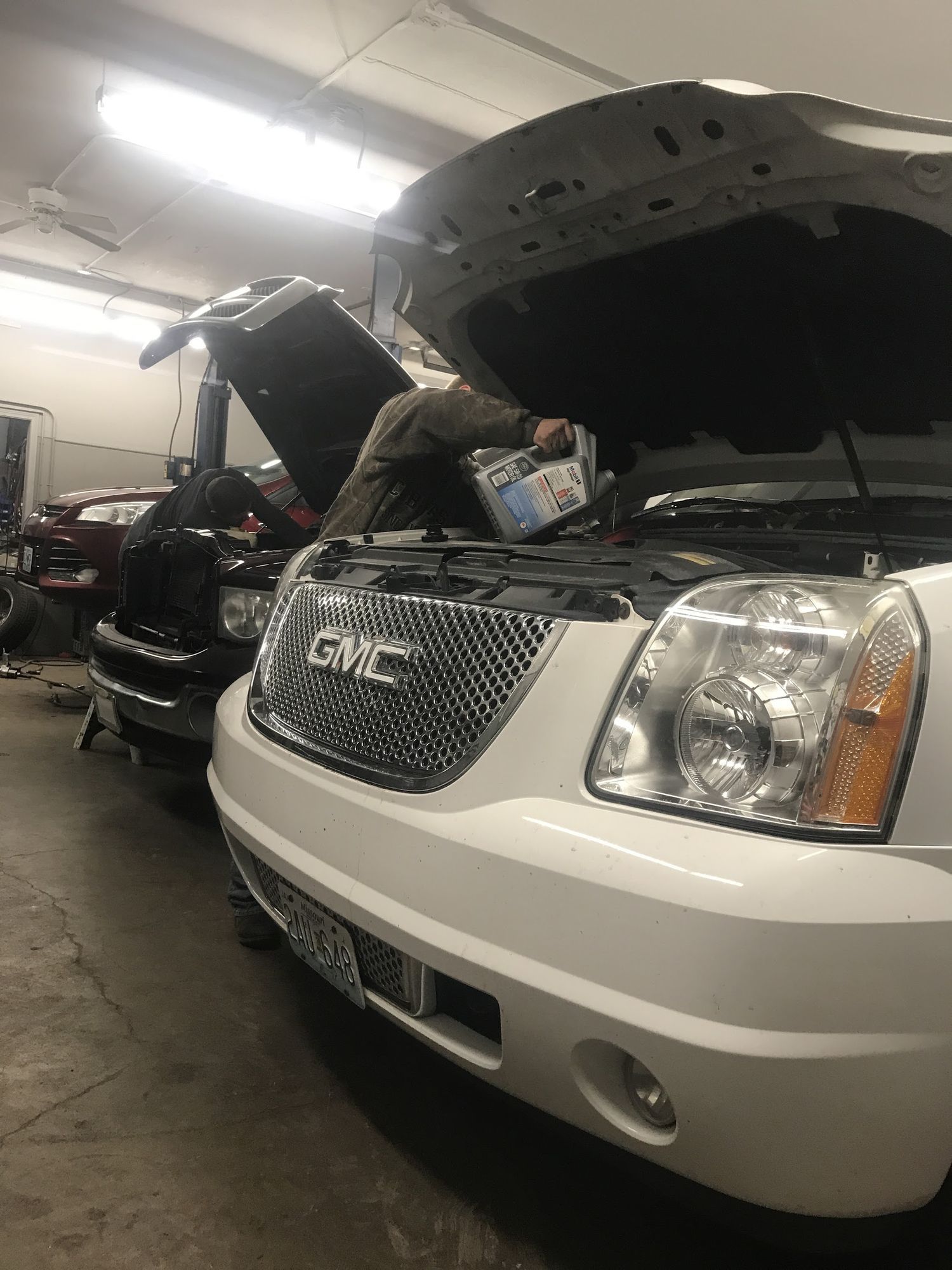 A mechanic pouring oil under the raised hood of an SUV inside Parker's Auto Repair